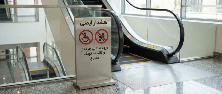 تابلو هشدار ممنوعیت استفاده از پله برقی برای معلولین و ویلچر در ورودی مجتمع تجاری