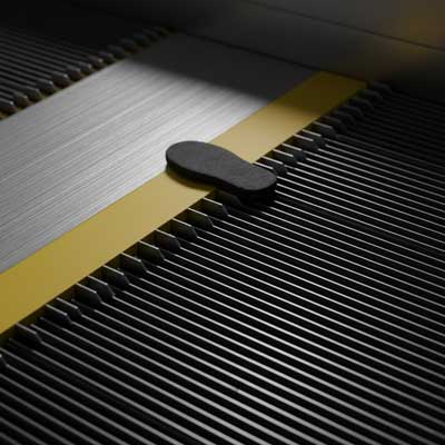 نمای نزدیک و با جزئیات از صفحه شانه پله برقی که خطر گیر افتادن در شکاف بین پله و سکو را نشان می‌دهد.