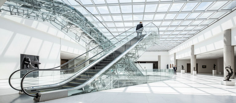 پله برقی تمام شیشه بدون فریم در آتریوم یک موزه مدرن و روشن