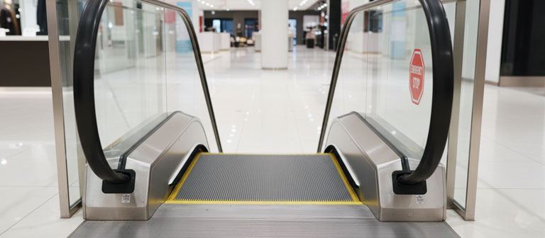 جزئیات ویژگی‌های ایمنی پله برقی شامل برس کناری و دکمه توقف اضطراری.