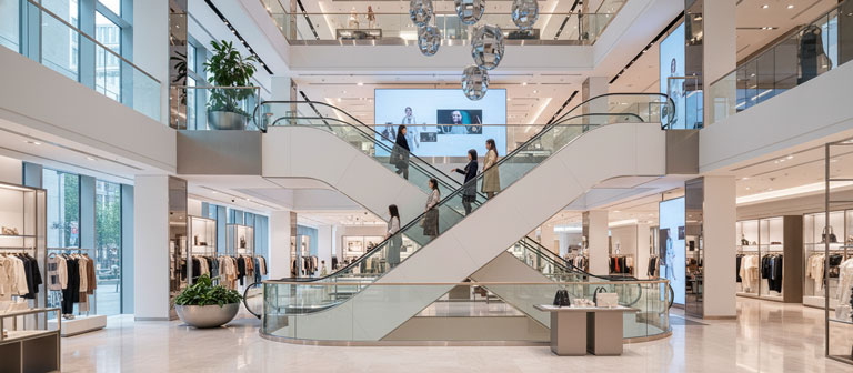 پله برقی فروشگاهی با نرده شیشه‌ای که مشتریان را به طبقه بالا هدایت می‌کند.